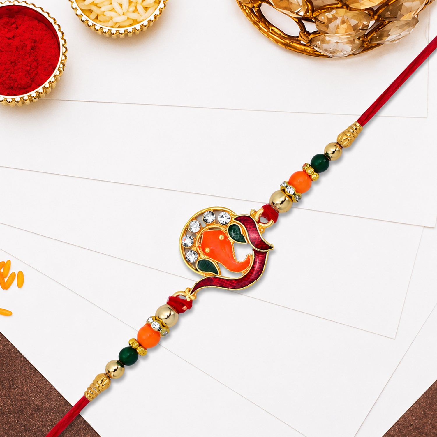 Golden Ganesha Rakhi with Red-Green Beads and Stone Detailing